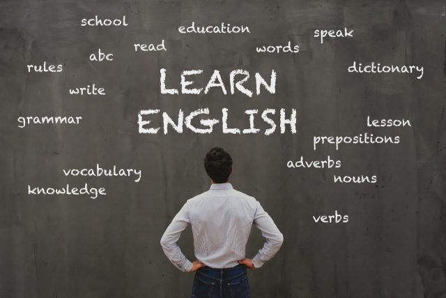 A man looks up at the words "learn English" written on a chalk board