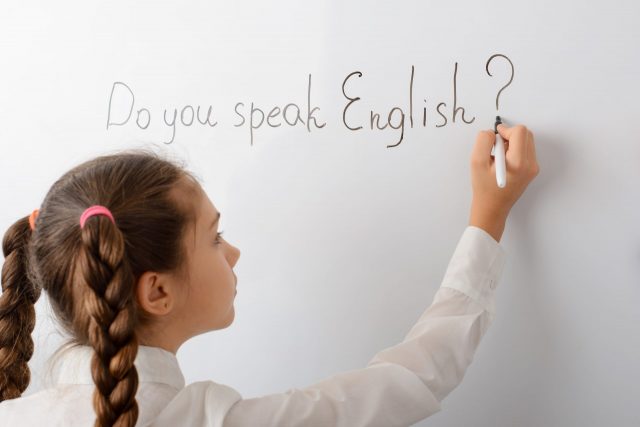 A girl writes on a whiteboard, "Do you speak English?"