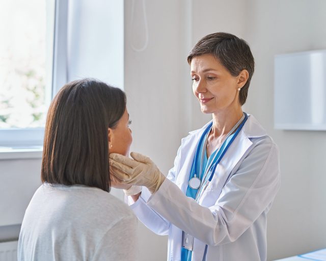 A doctor examines her patient's mouth and neck 