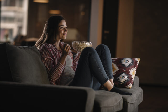 Woman enjoys watching TV with popcorn.