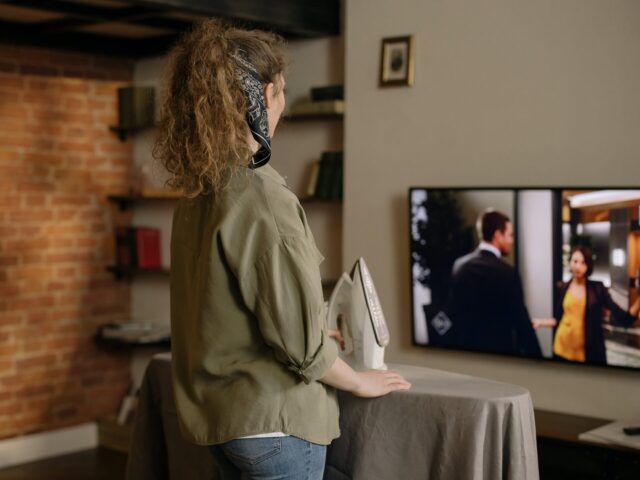 A woman watches English TV while she does chores.
