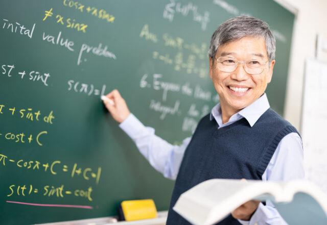 A professor writes equations on a chalk board.